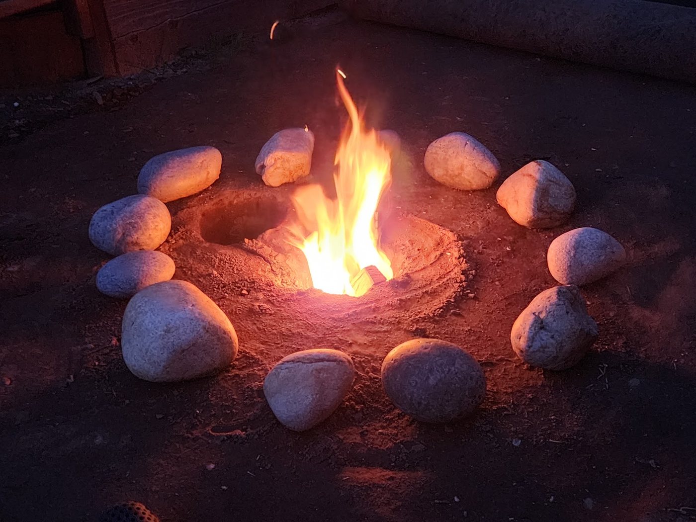 A ring of river stones around a small fire at dusk