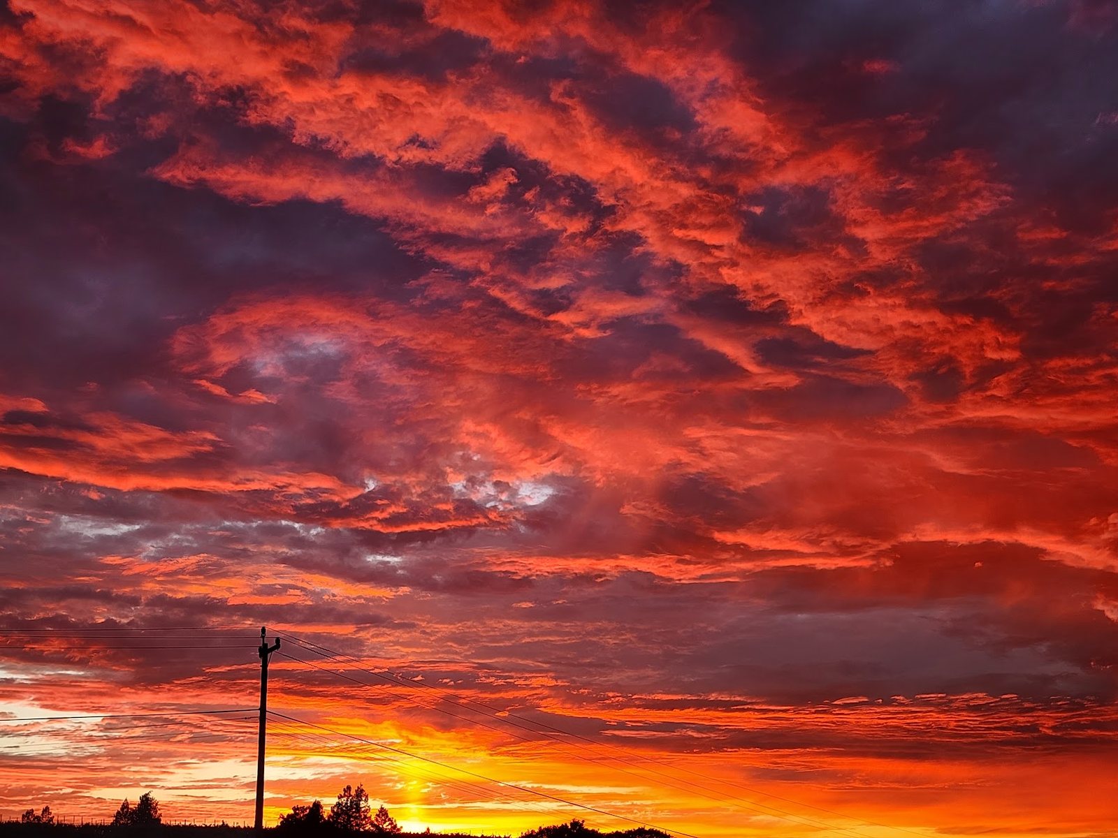 Power lines and a pole silhouetted against a red sunset